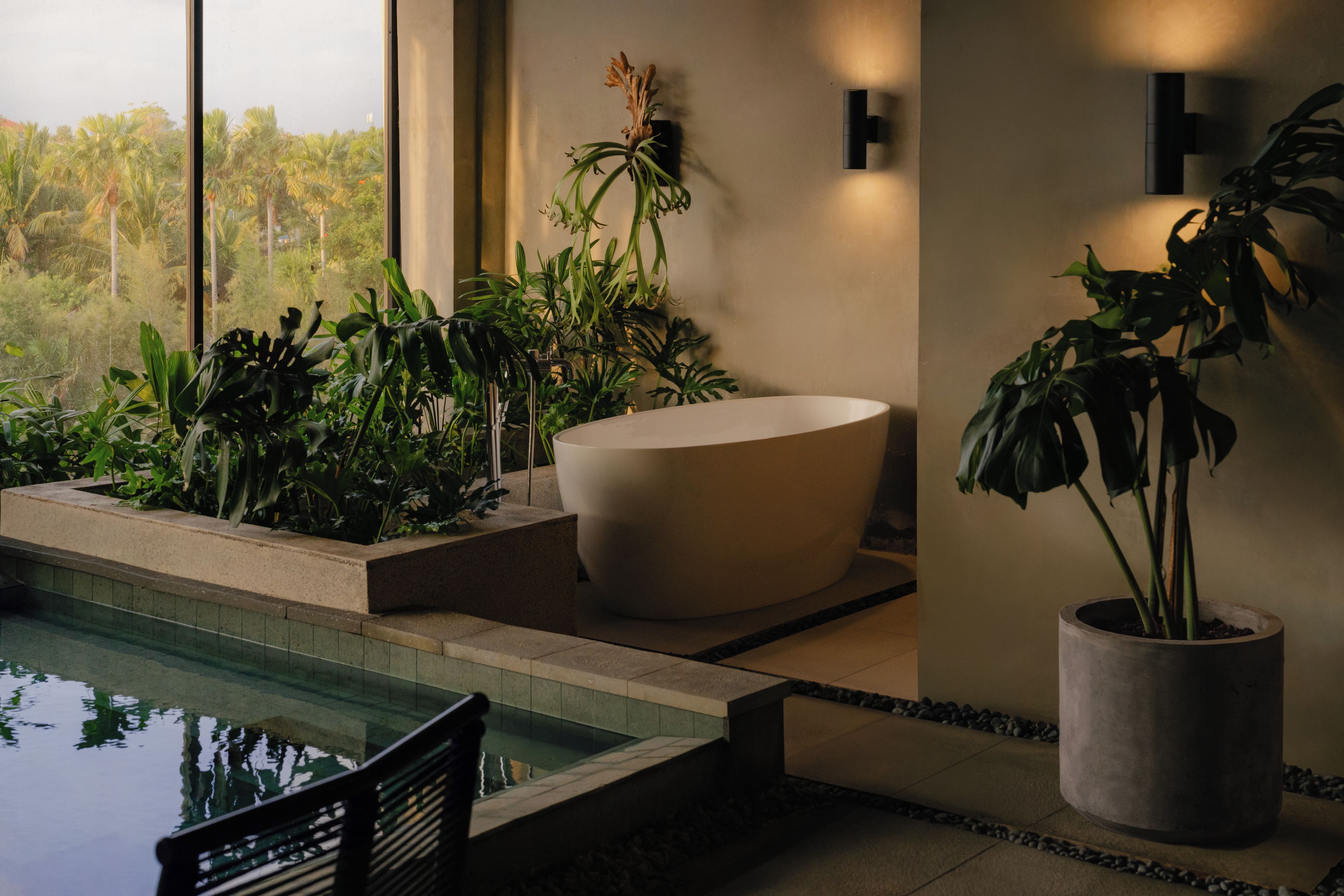 Un baño moderno con una bañera grande, una planta en maceta y vistas a un paisaje tropical.