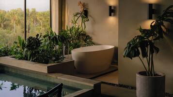 Un baño moderno con una bañera grande, una planta en maceta y vistas a un paisaje tropical.