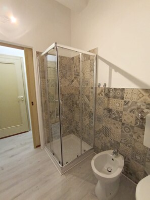 Un baño con ducha envuelta en vidrio, un bidé y baldosas con diseño.