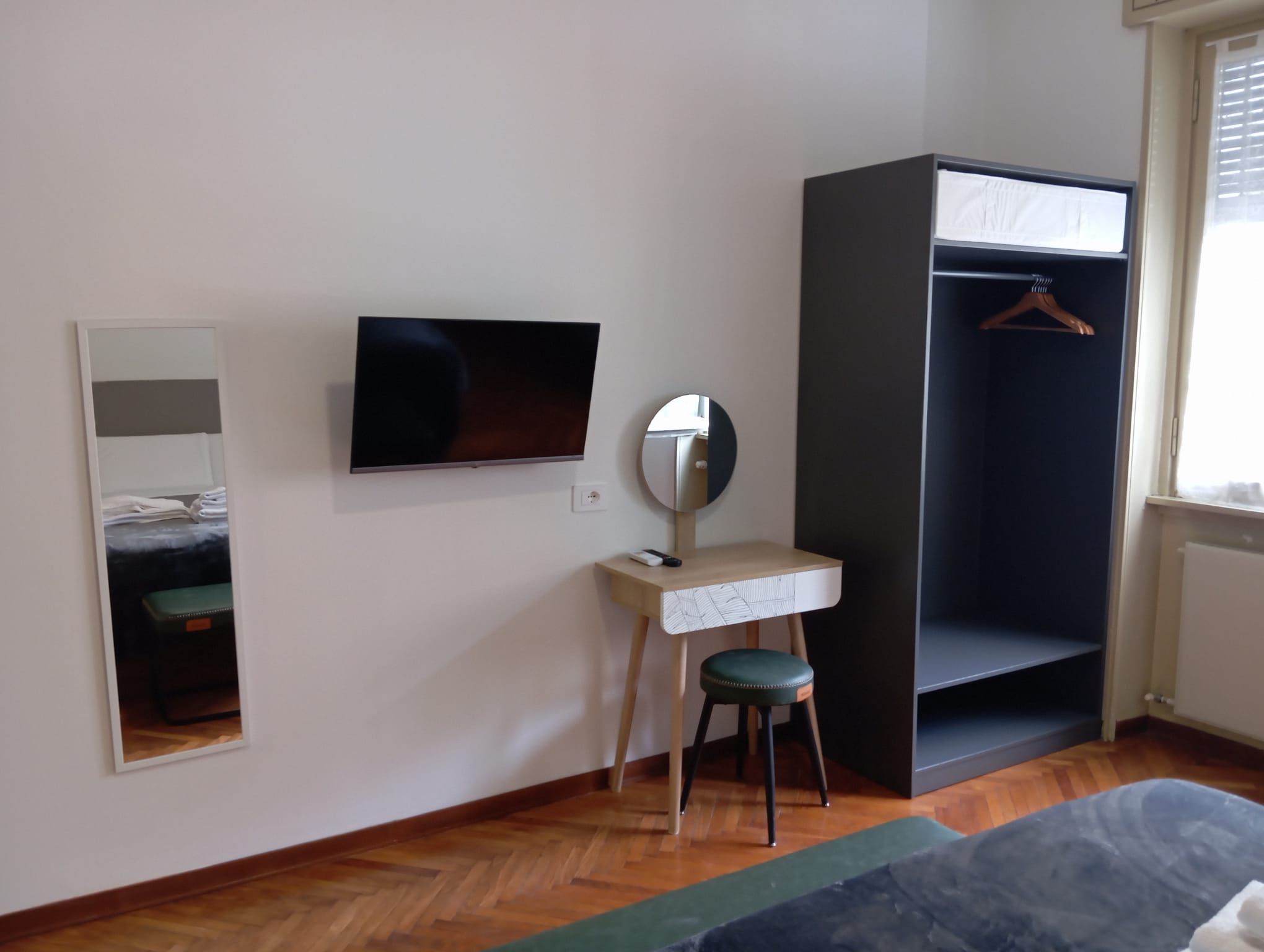 Ein Zimmer mit einem Bett, einem Schreibtisch mit Stuhl, einem Fernseher, einem Kleiderschrank und einem Spiegel.