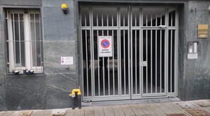 Una entrada protegida por un portón, con un cartel de 'prohibido estacionar', un letrero de advertencia y una placa con el número del edificio.