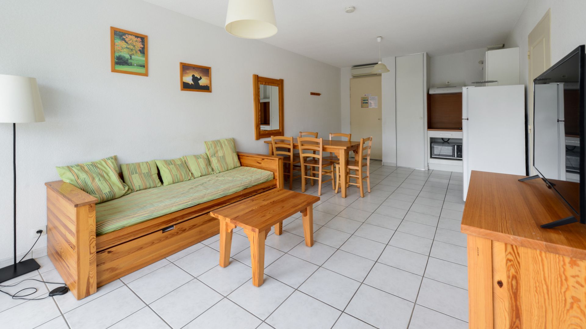 A modern living room with a sofa, coffee table, and dining set. There is a kitchen area with a refrigerator and microwave.