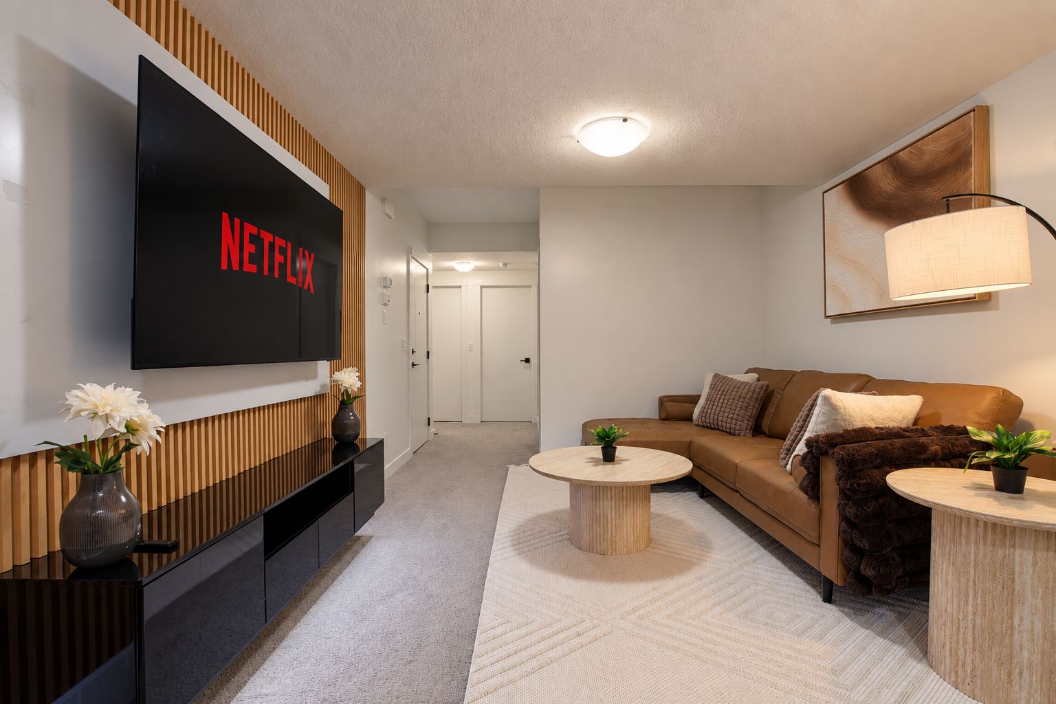 A modern living room with a flat-screen TV displaying 'NETFLIX,' a sofa, two coffee tables, and a potted plant.