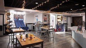 Una habitación acogedora y bien iluminada, con un aro de baloncesto, mesas con material de arte y un mostrador de snacks.