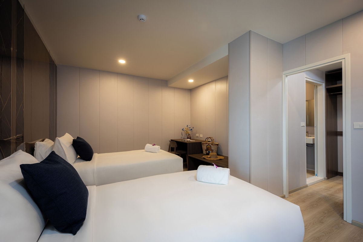 A hotel room with two beds, a desk, a chair, and a wardrobe.