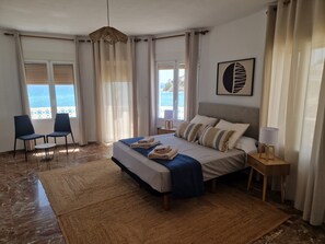 Ett sovrum med en säng, två stolar, ett nattduksbord, en lampa och utsikt över havet.