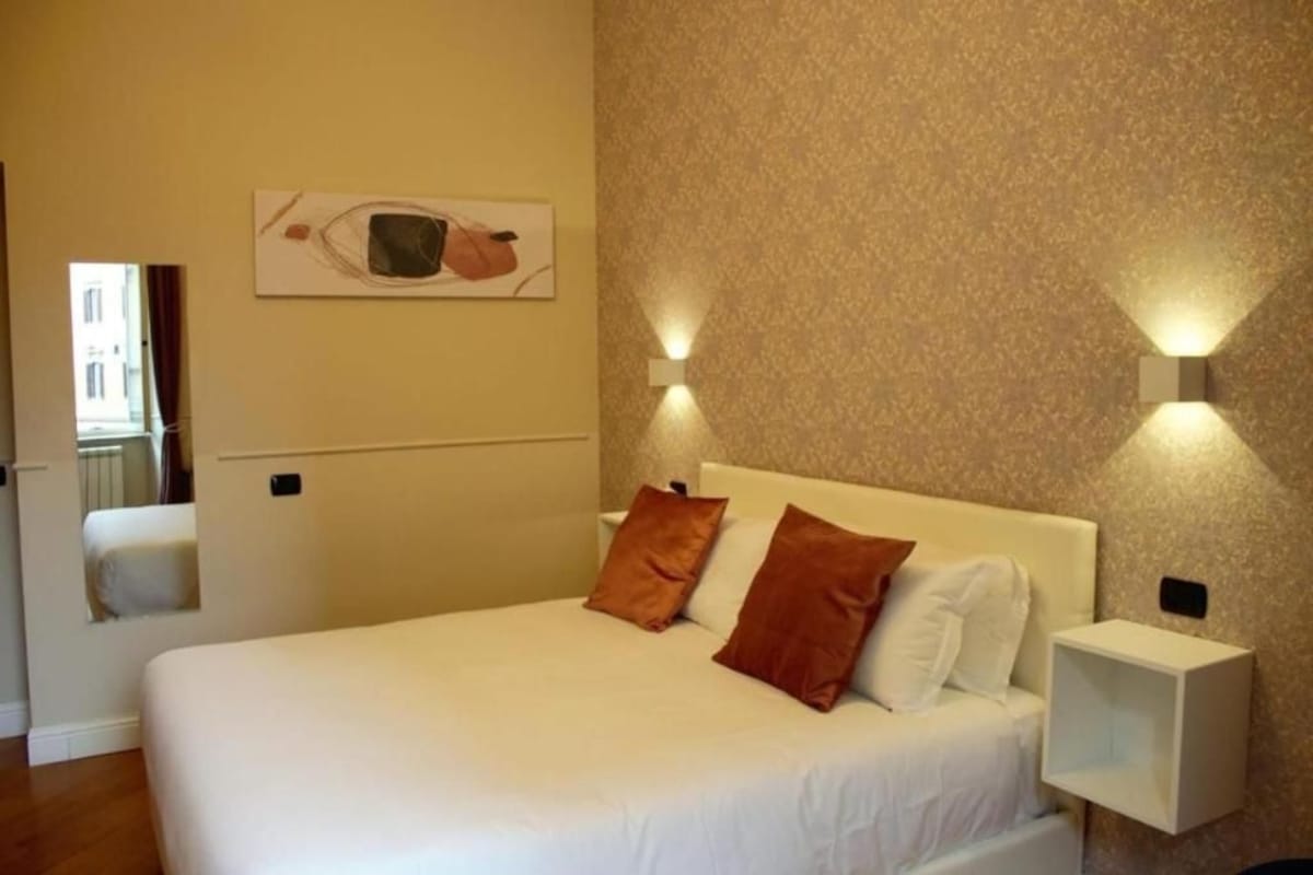 A hotel room with a bed, two wall-mounted lights, a nightstand, and a painting on the wall.