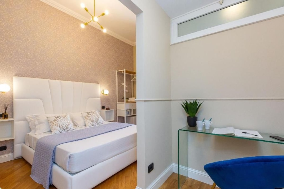 A modern bedroom with a bed, bedside tables, a glass shelf with toiletries, and a shower area.