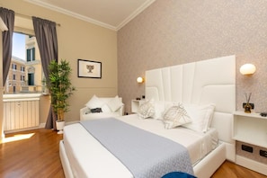 A hotel room with a large bed, a potted plant, a framed picture on the wall, and a view of buildings outside. - 52 Vespasiano Vatican Suites (Roma)