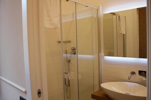 Un baño con cabina de ducha de vidrio, un lavabo blanco y un espejo.