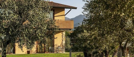 A building with a balcony, surrounded by trees and a grassy area.