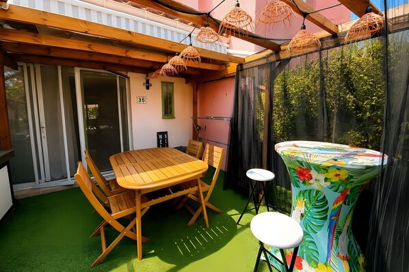 Eine Terrasse im Freien mit einem Holztisch und Stühlen, einem kleinen runden Tisch und einem bunten Sonnenschirm.