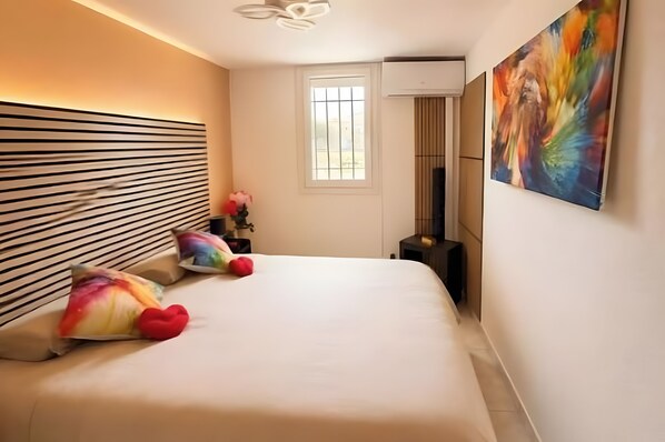 A modern bedroom with a large bed, a window, and a painting on the wall.