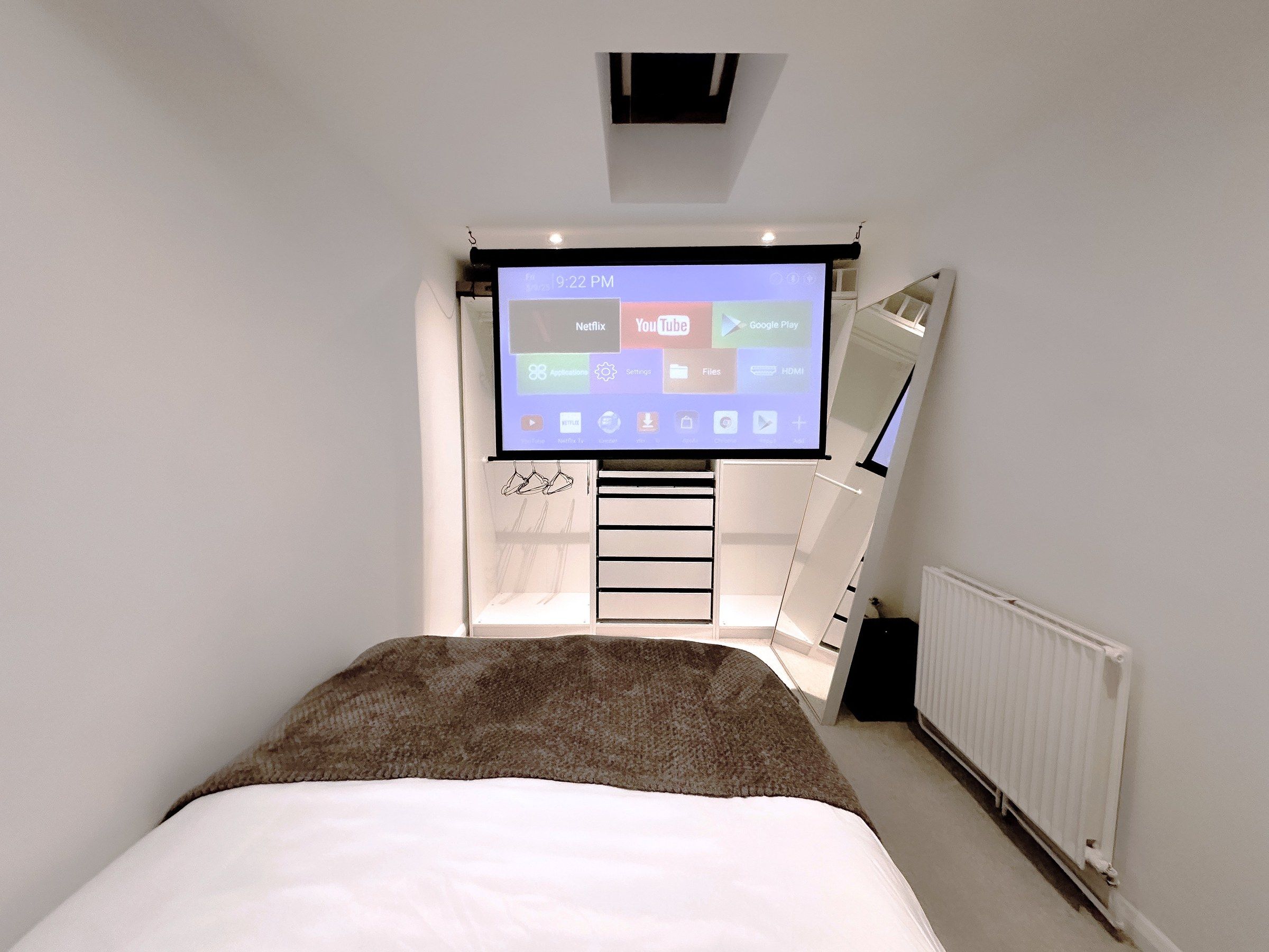 Un dormitorio con cama, televisor montado en la pared y una escalera que lleva a un altillo.