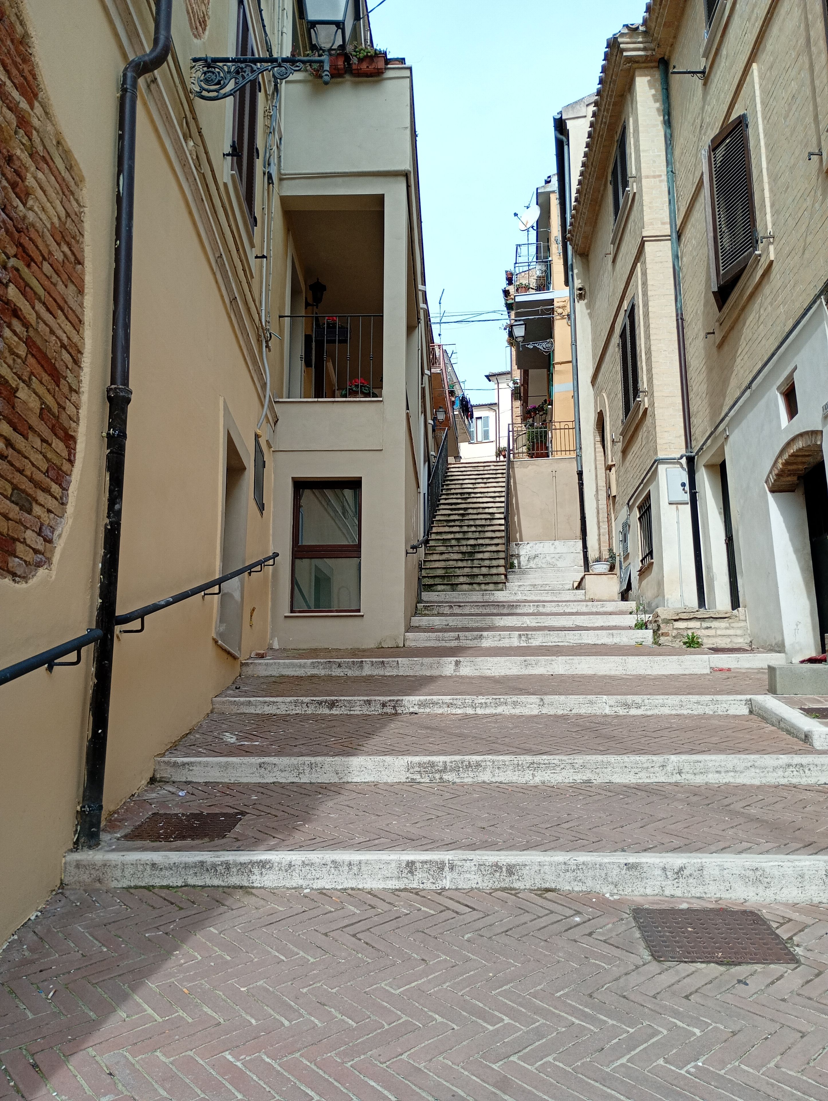 A narrow street with a staircase leading to a building with a balcony.