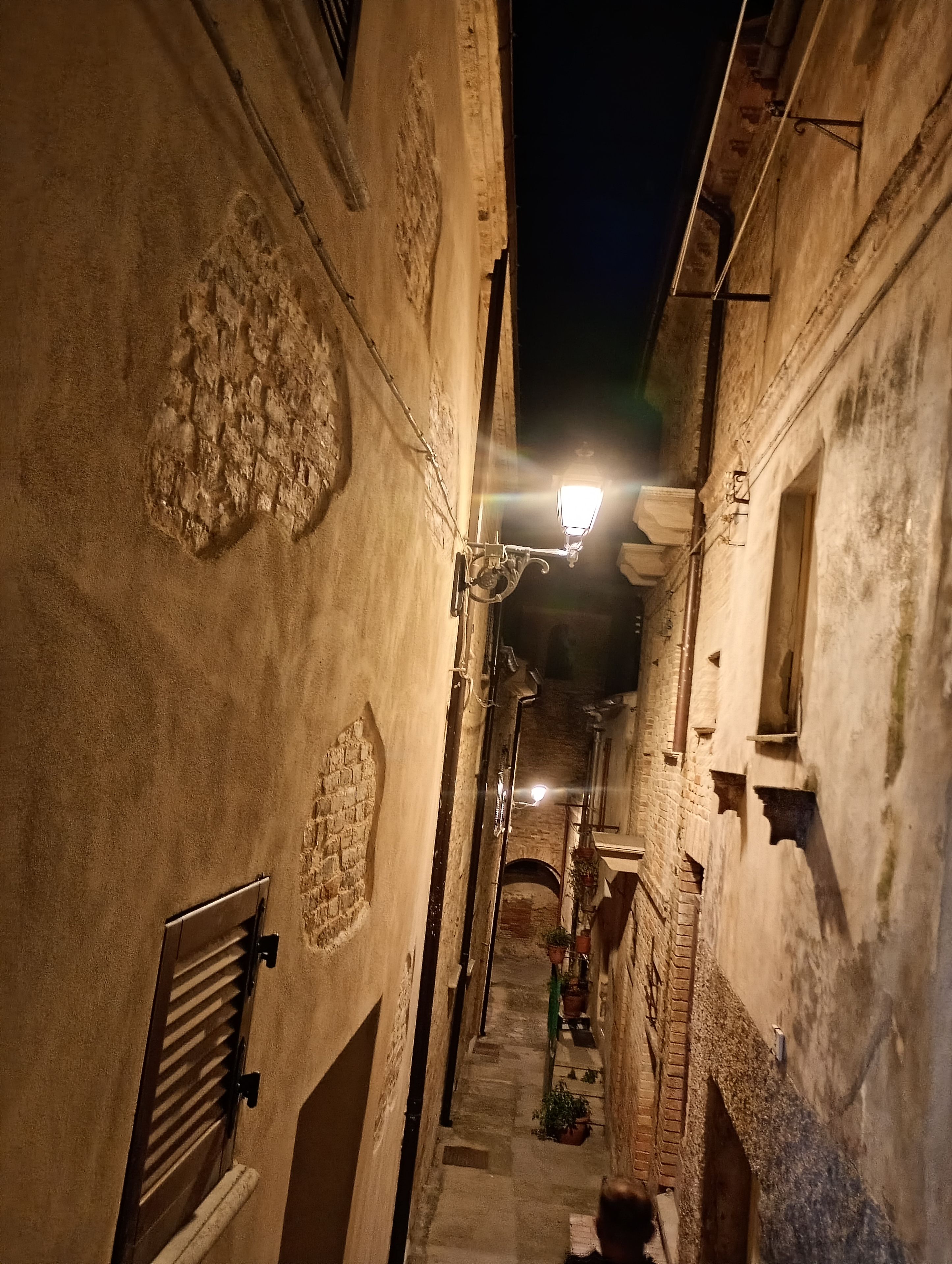Um beco estreito com paredes de pedra e um único poste de luz iluminado.