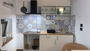 A kitchen with a tiled backsplash, a black range hood, a white cabinet with a glass shelf above, and a wicker chair. - Al Borgo Da Rita (Città S Angelo)