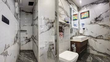A bathroom with a shower, toilet, and sink, all with marble flooring and walls.