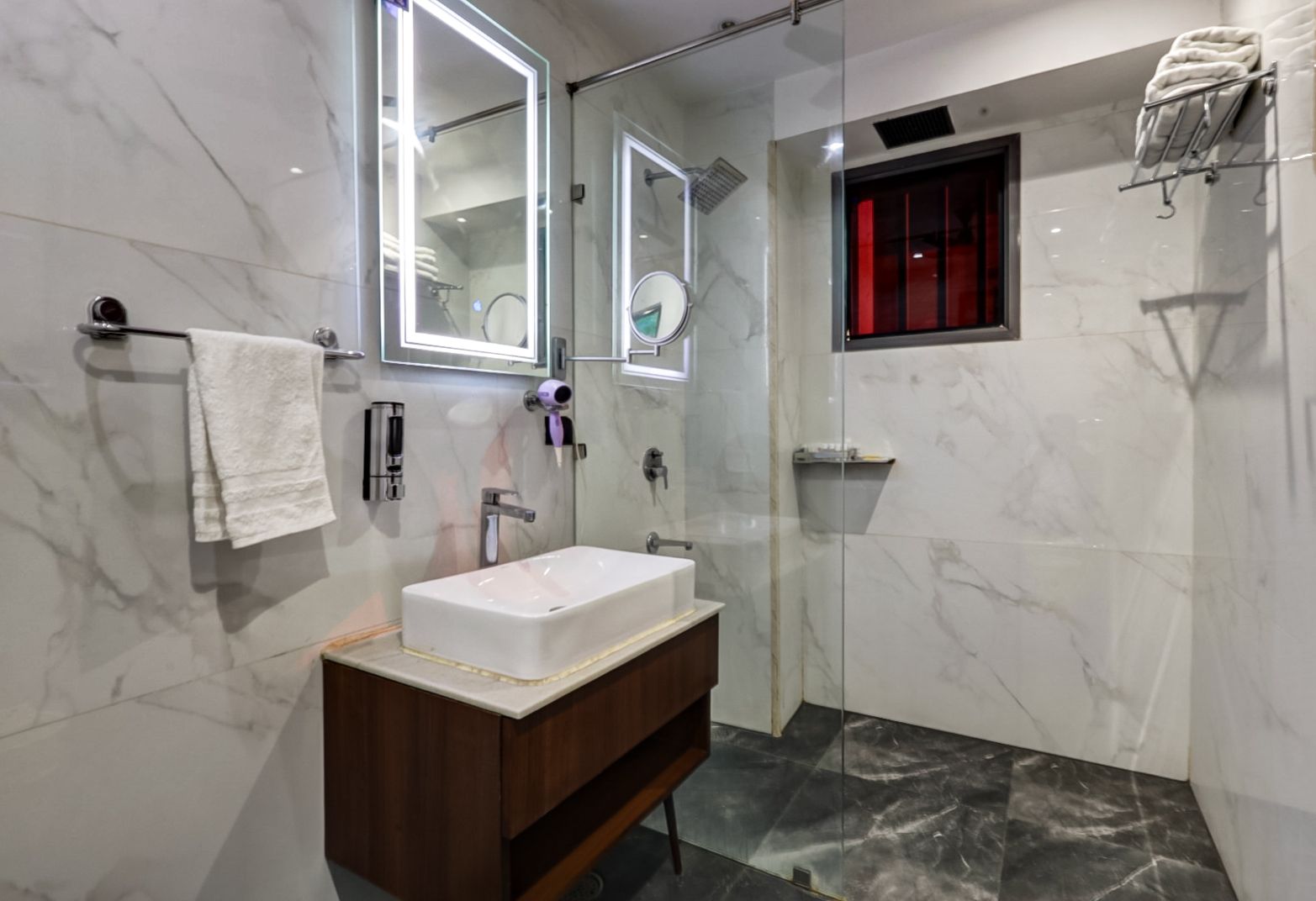 A modern bathroom with a marble vanity, a large mirror, a handheld showerhead, and a towel rack.