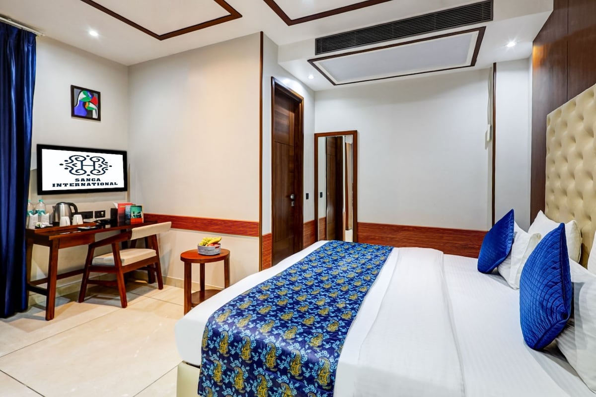A hotel room with a bed, a desk, a chair, a small table with fruits, and a television.