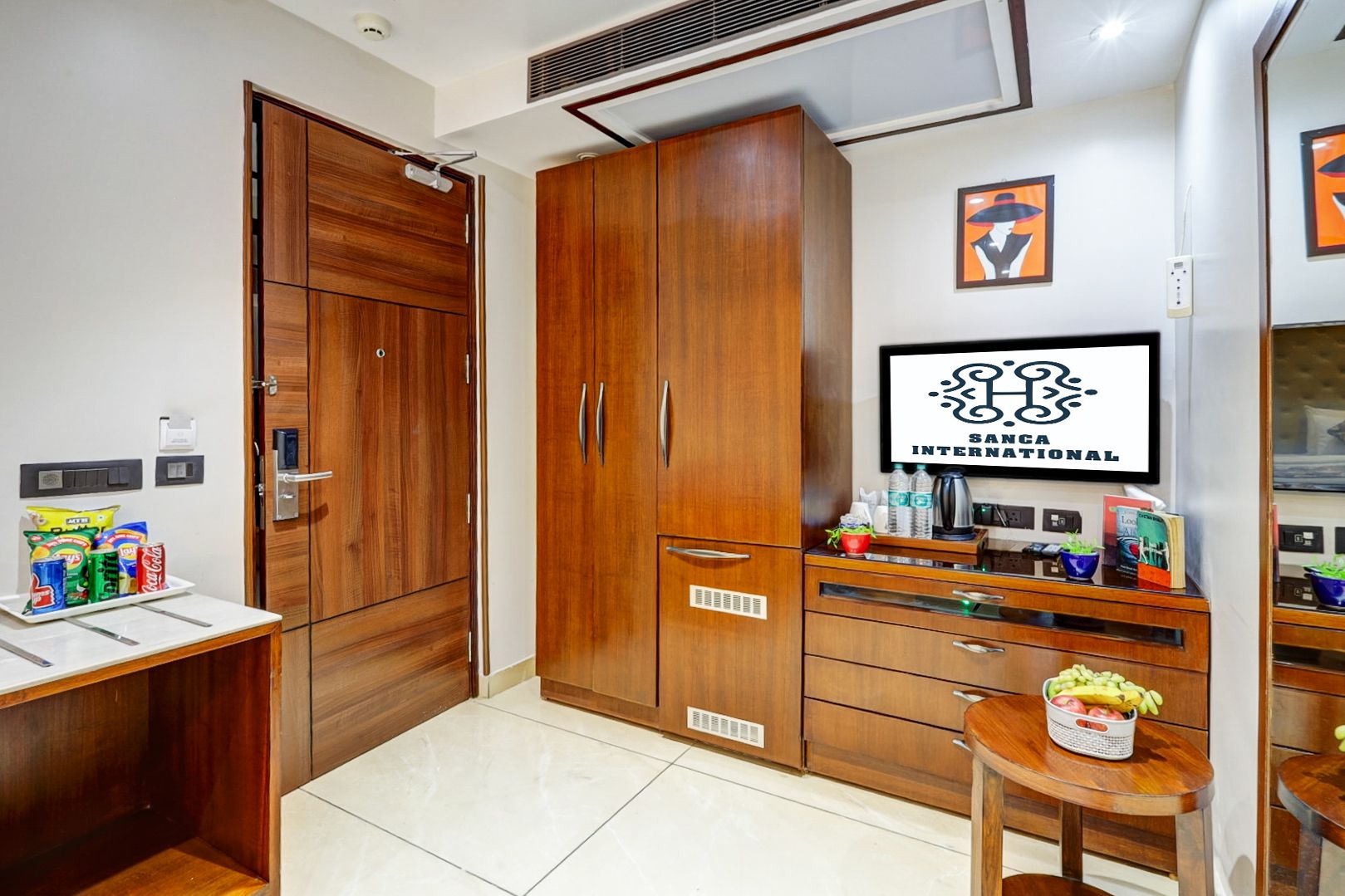 Una habitación de hotel con un armario de madera, una mesita con aperitivos, un televisor y una obra de arte colgada en la pared.