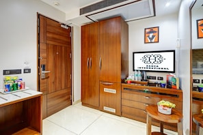 A hotel room with a wooden wardrobe, a small table with snacks, a television, and a wall-mounted artwork. - Sanca International Patel Nagar New Delhi (New Delhi)