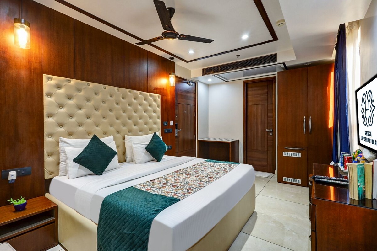 A hotel room with a large bed, a ceiling fan, wooden wardrobe, and a desk with a chair.