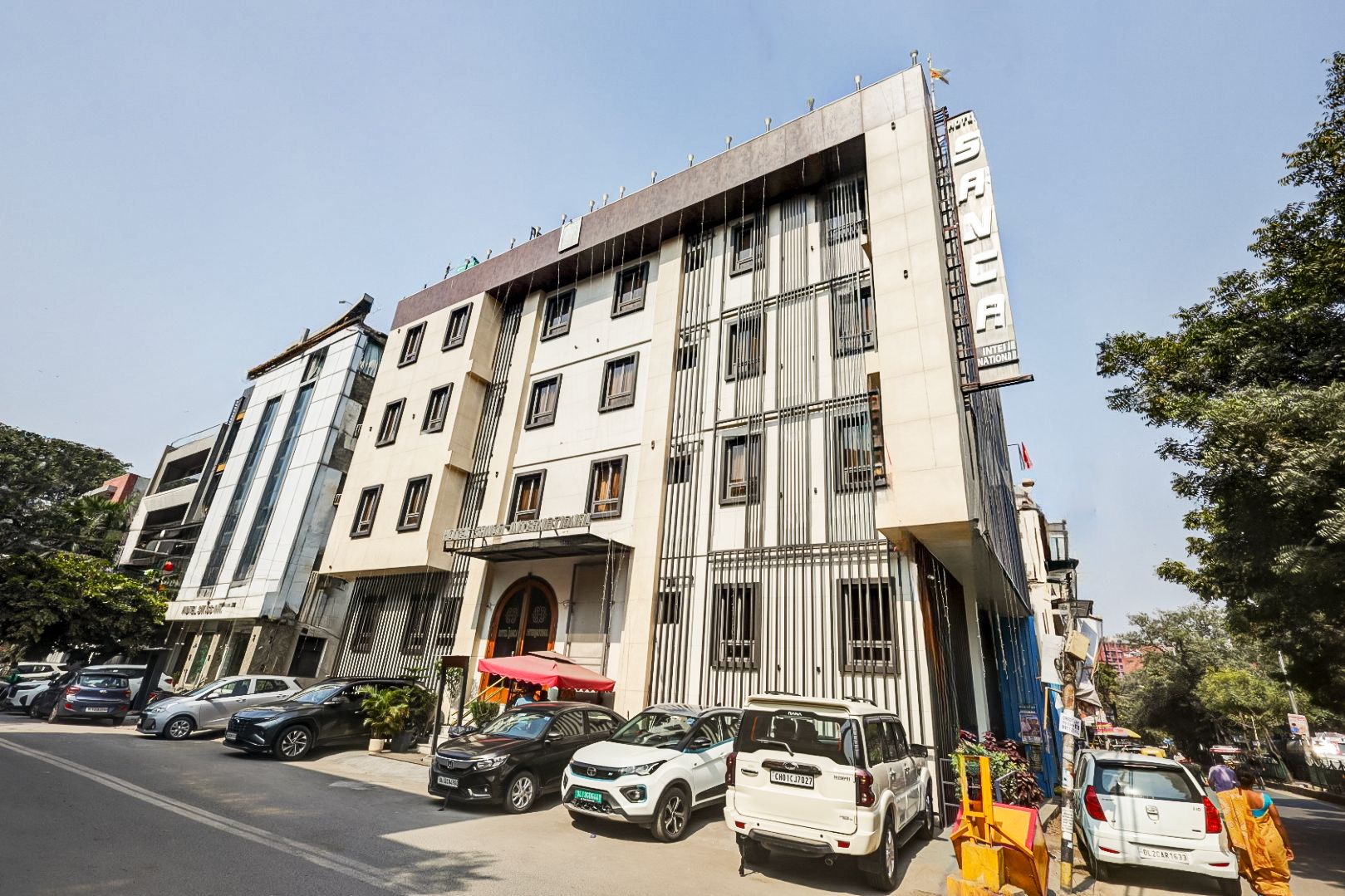 A multi-story building with a prominent entrance, several parked cars, and a clear sky.