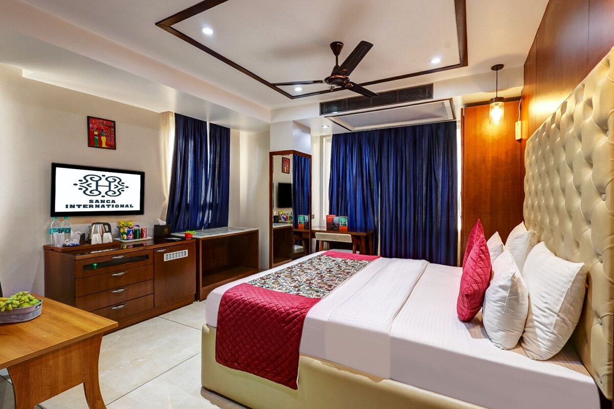A hotel room with a bed, a desk, a chair, a wardrobe, a ceiling fan, and a television.