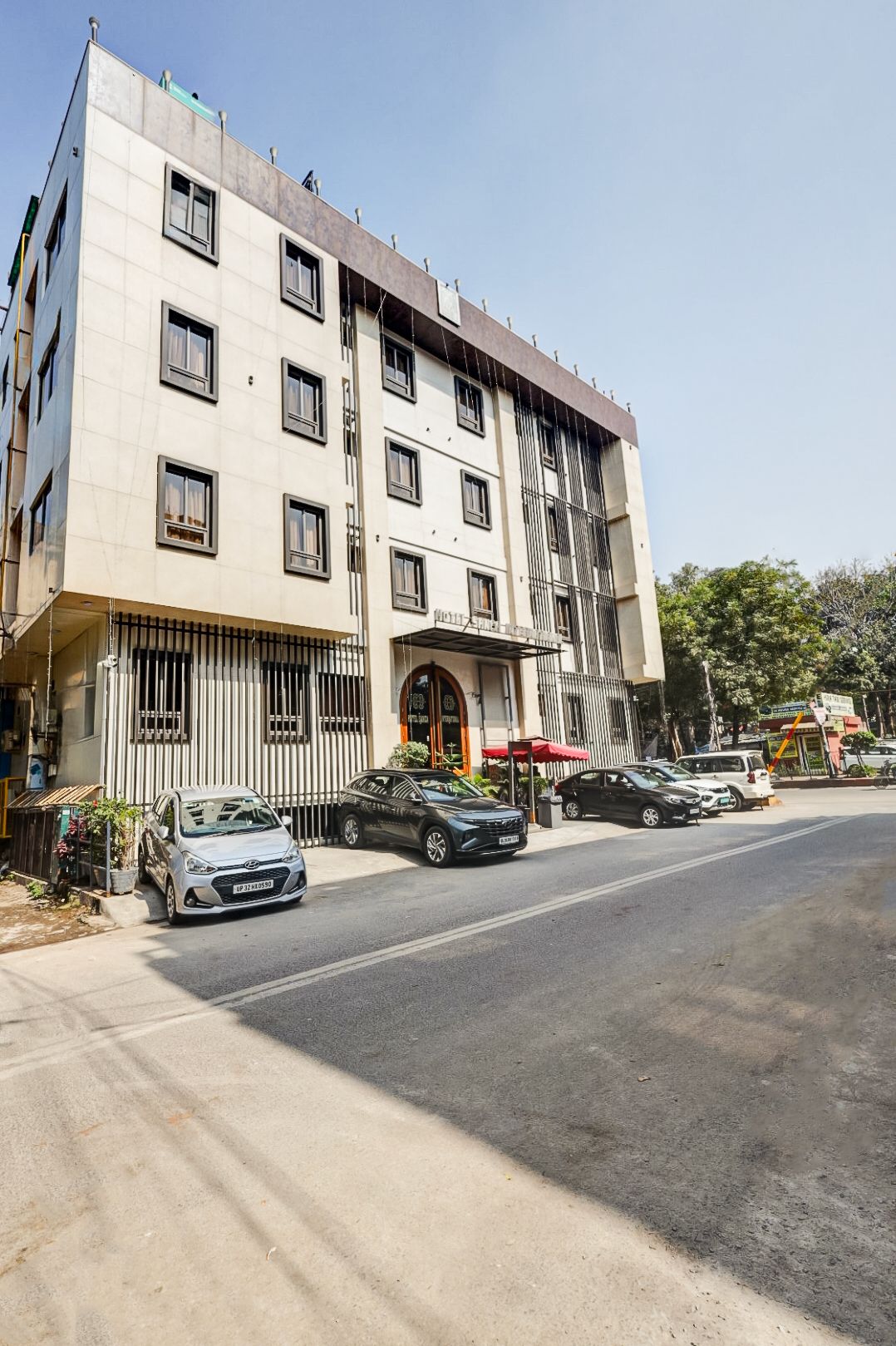 Un hotel de varios pisos con fachada moderna, un acceso cubierto y un estacionamiento con varios automóviles.