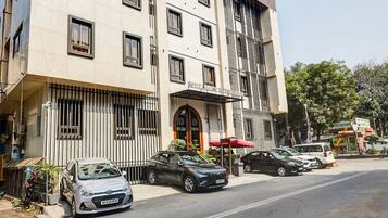 Un hotel de varios pisos con fachada moderna, un acceso cubierto y un estacionamiento con varios automóviles.