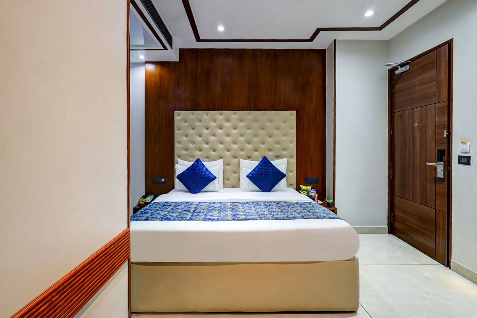 Habitación de hotel con una cama grande, paneles de madera en las paredes, un armario de madera y un diseño de techo moderno.