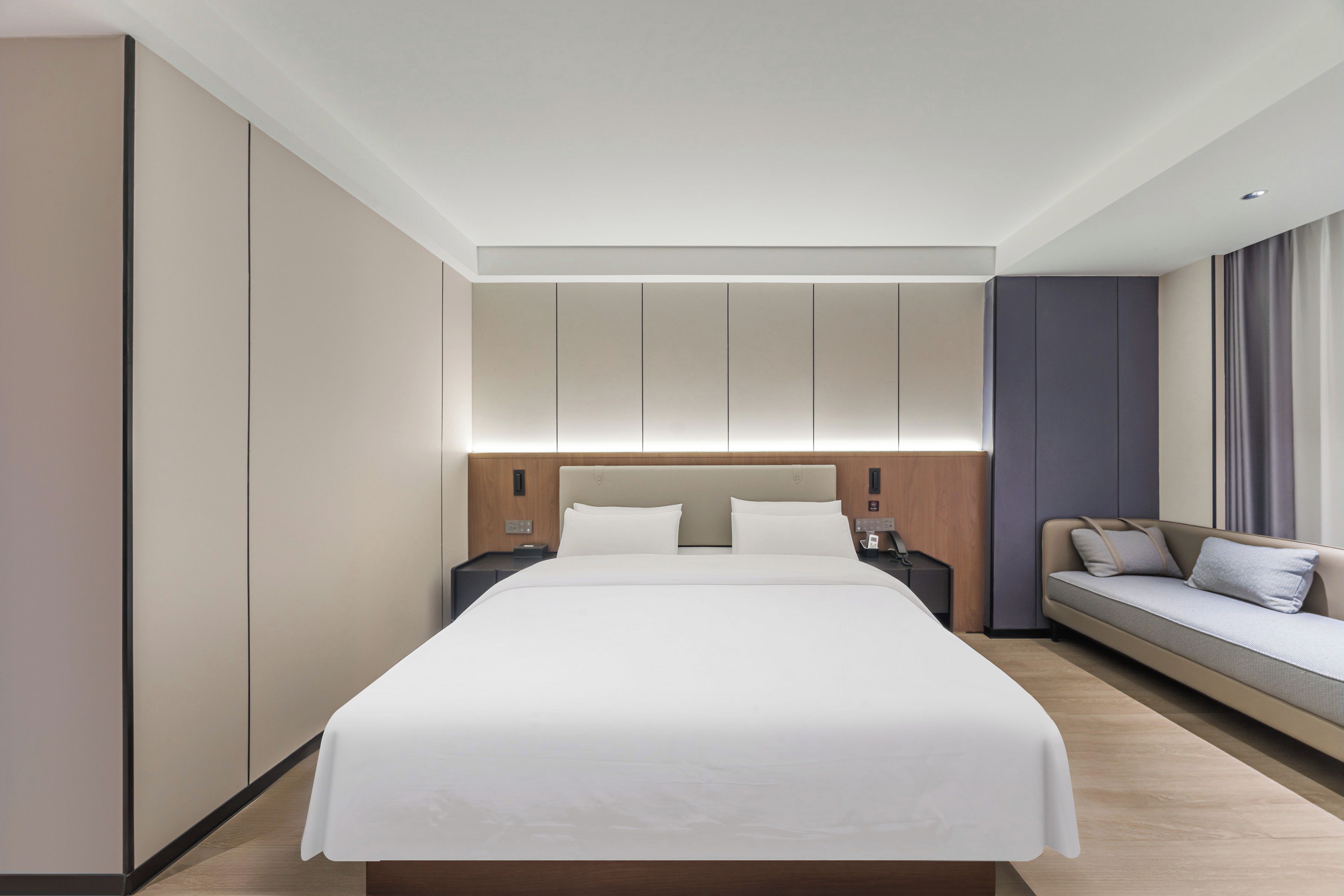 A modern hotel room with a large bed, a sofa, and a nightstand.