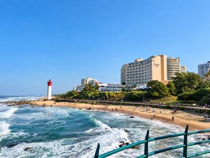 A coastal hotel with a prominent lighthouse, beachfront, and ocean waves. - 3-Bedroom Beachfront Apartment with Ocean Views & Pool – Umhlanga Rocks (uMhlanga)