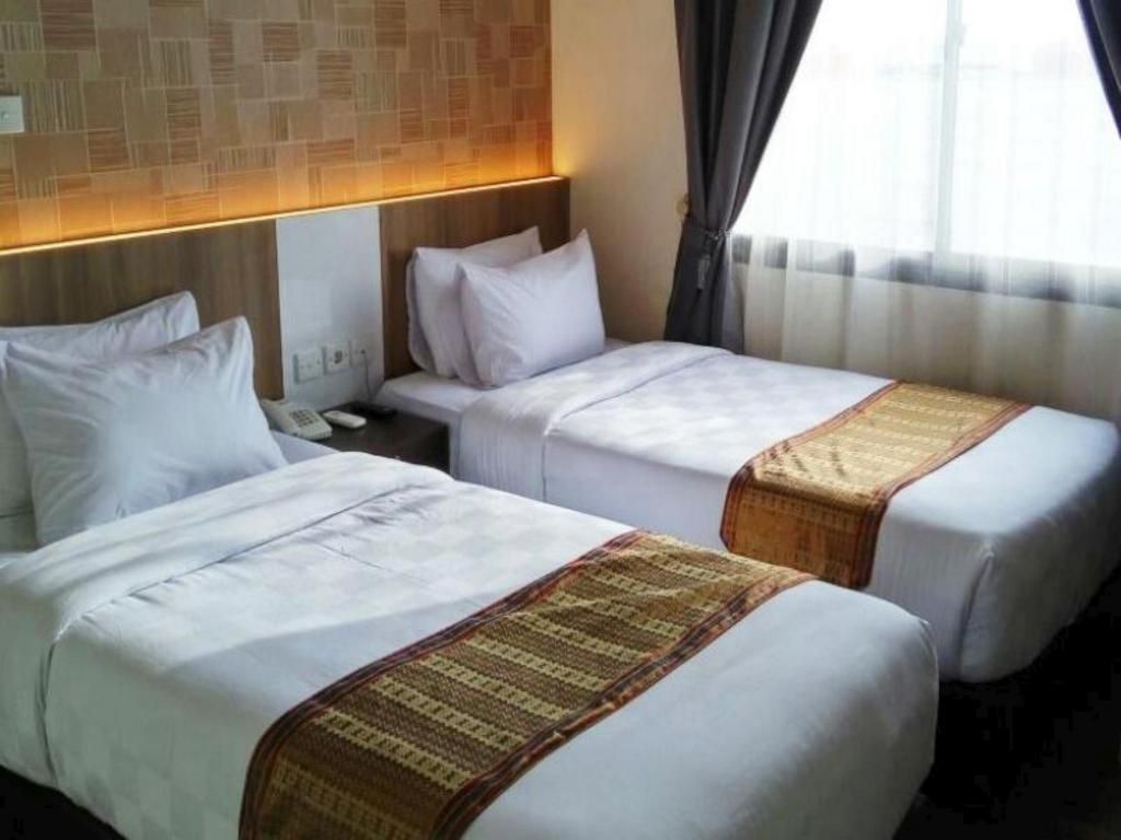 A hotel room with two single beds, a headboard with a patterned design, a bedside table with a phone, and a window with curtains.