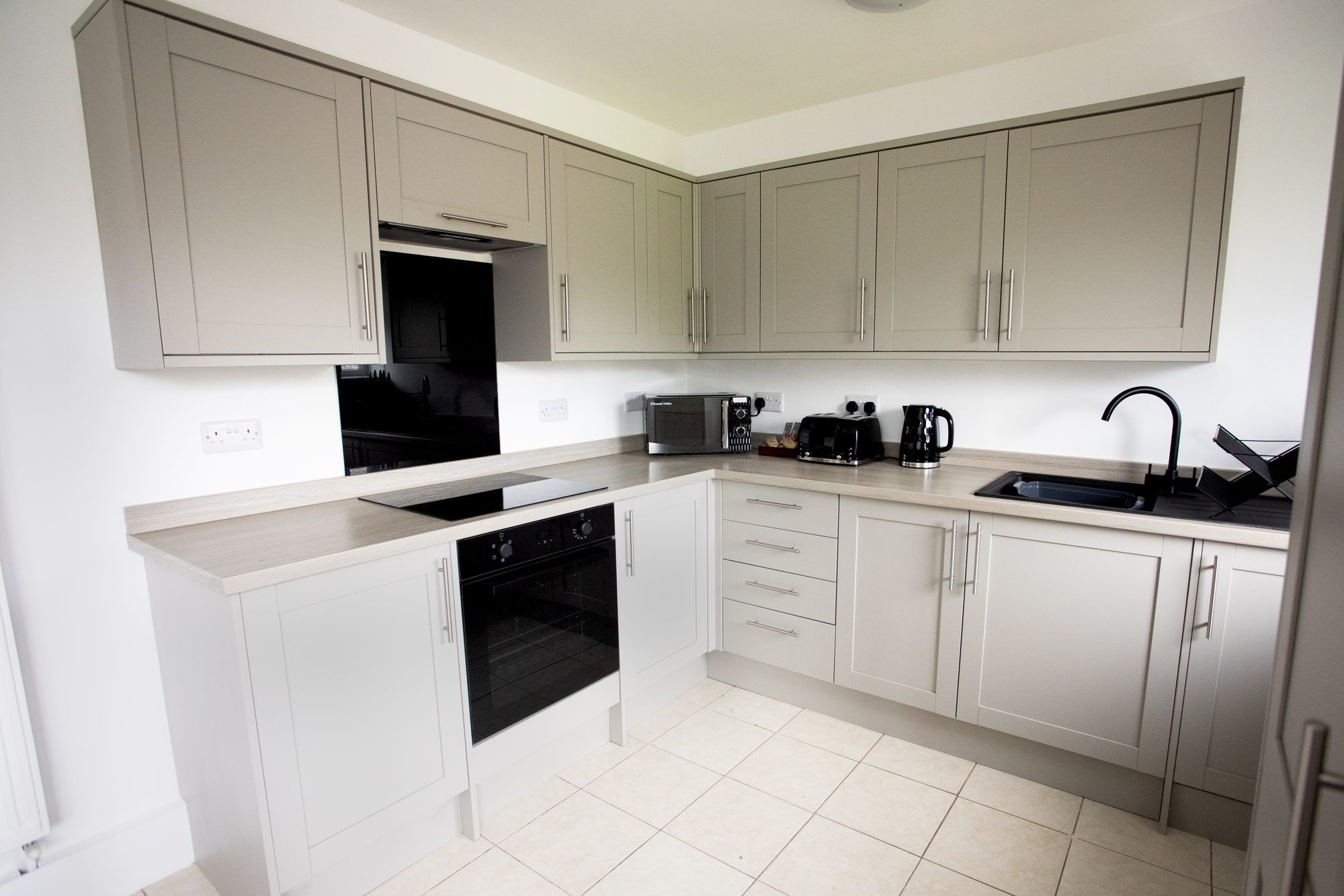 A modern kitchen with light-colored cabinets, a black oven, a toaster, and a sink.