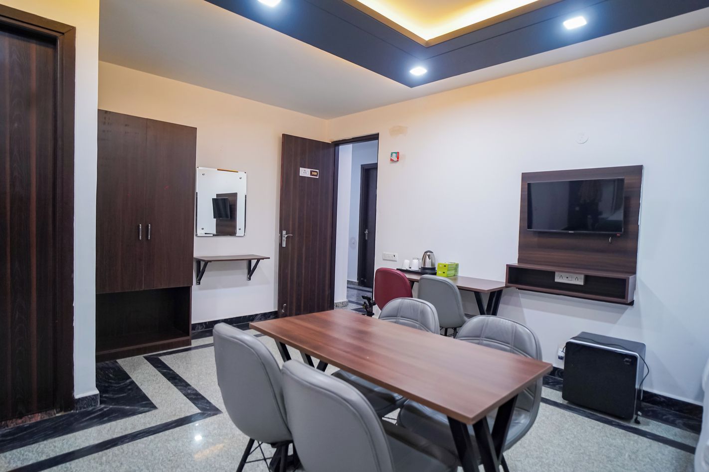 Un salón de conferencias con una mesa de madera, seis sillas, un televisor y una pequeña área de cocina.