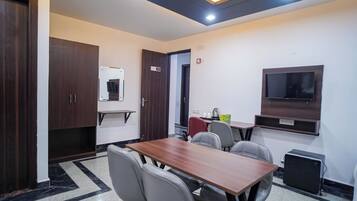 Un salón de conferencias con una mesa de madera, seis sillas, un televisor y una pequeña área de cocina.