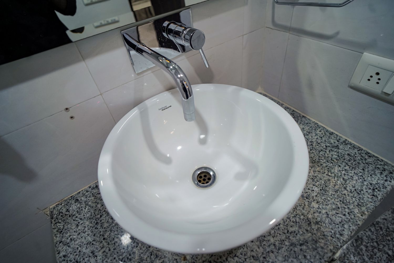 Un lavabo blanco con grifo cromado y desagüe, sobre una encimera de granito.