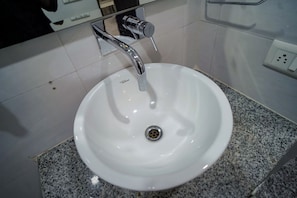A white bathroom sink with a chrome faucet and a drain, set on a granite countertop. - Norvale Stays (Gurugram)