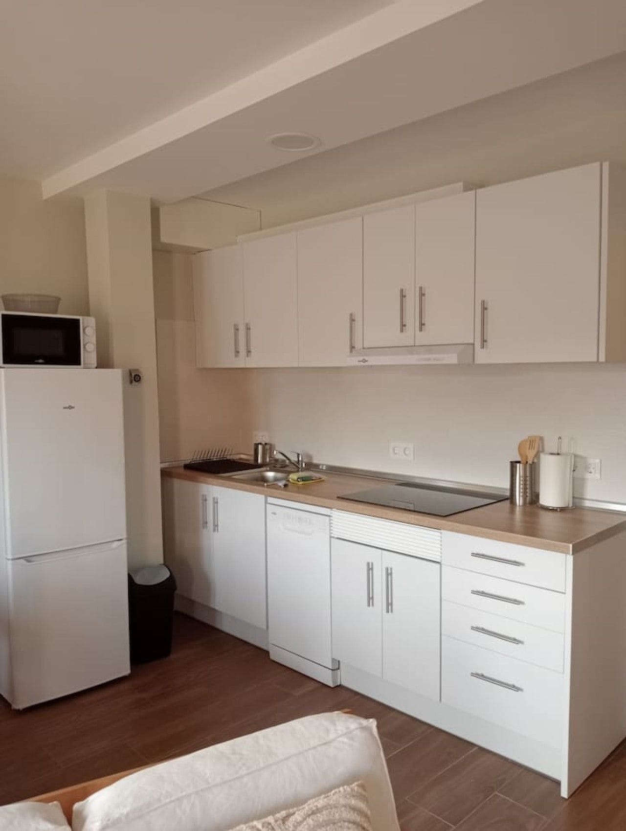 Een kleine keuken met witte kastjes, een magnetron en een spoelbak.
