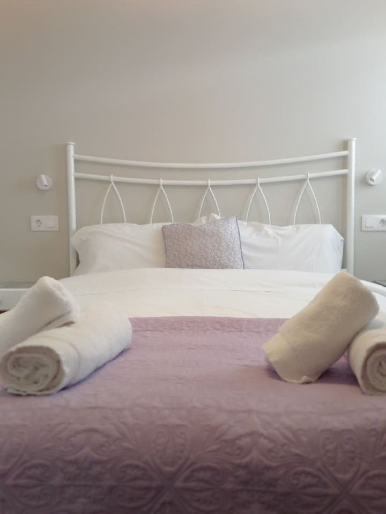 Un lit avec du linge de lit blanc, une couvre-lit violette et deux serviettes enroulées.