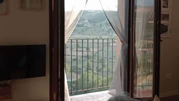 Une pièce dotée d’une grande porte-fenêtre coulissante donnant sur un balcon avec vue sur un paysage vallonné.