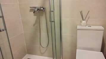 Un baño con ducha de vidrio, inodoro blanco y un estante pequeño con un difusor de aroma de caña.