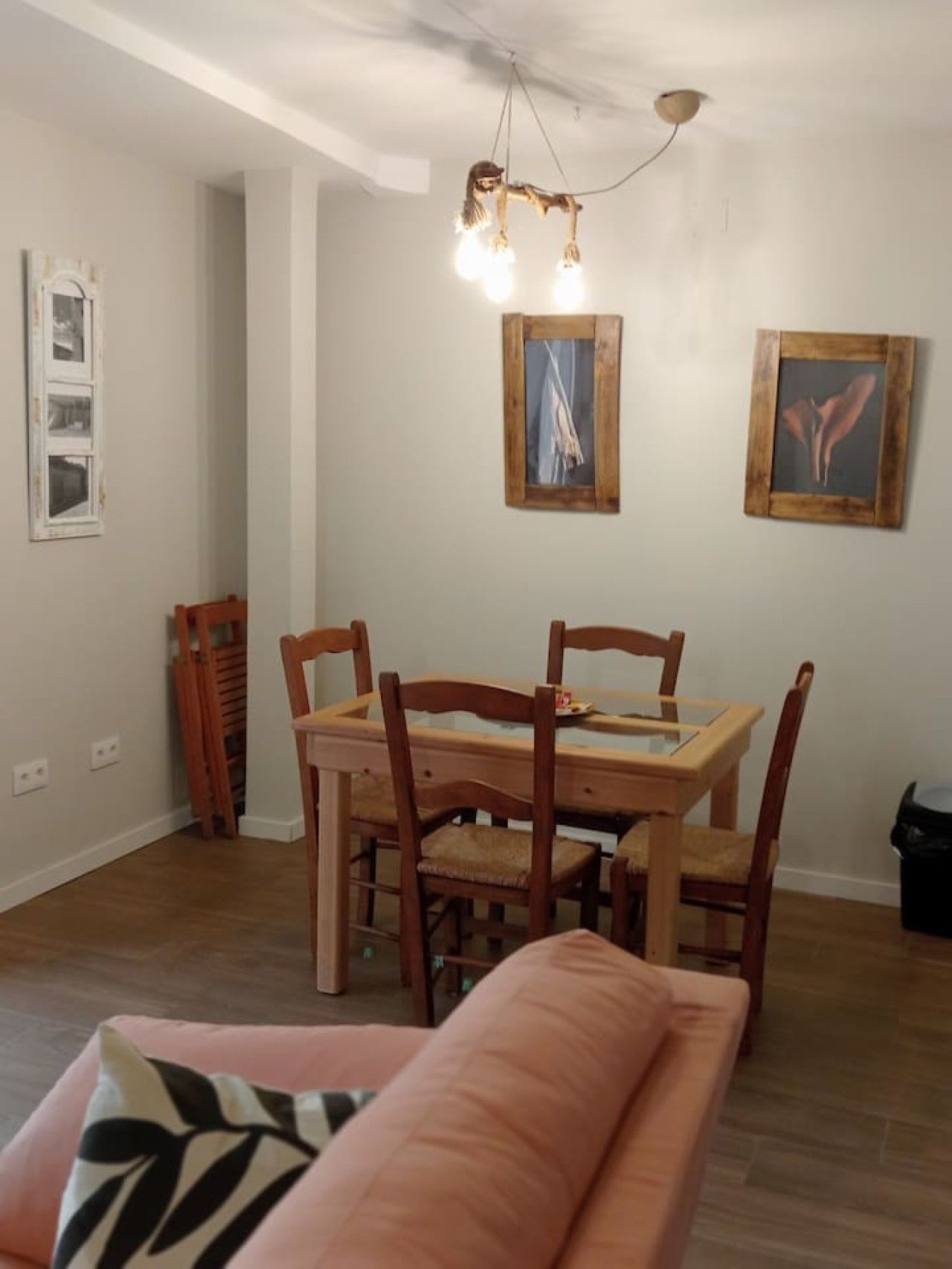 Un coin repas avec une table et des chaises en bois, un luminaire suspendu et deux tableaux encadrés au mur.