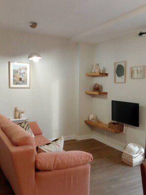 A living room with a sofa, a flat-screen TV mounted on the wall, and decorative shelves. - Casa Cántara Morería | Winter in the Maestrazgo   (Tronchón)