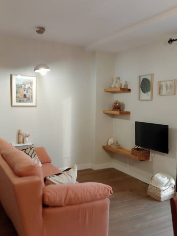 A living room with a sofa, a flat-screen TV mounted on the wall, and decorative shelves. - Casa Cántara Morería | Winter in the Maestrazgo (Tronchón)