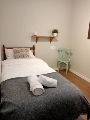 A bedroom with a bed, a chair, a shelf with a plant, and a towel on the bed. - Casa Cántara Morería | Winter in the Maestrazgo (Tronchón)