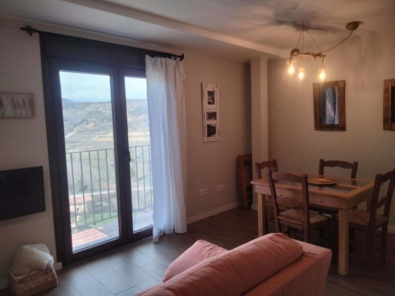 Una habitación con puerta de vidrio corredera que da a un balcón, una mesa de comedor con sillas y un sofá.