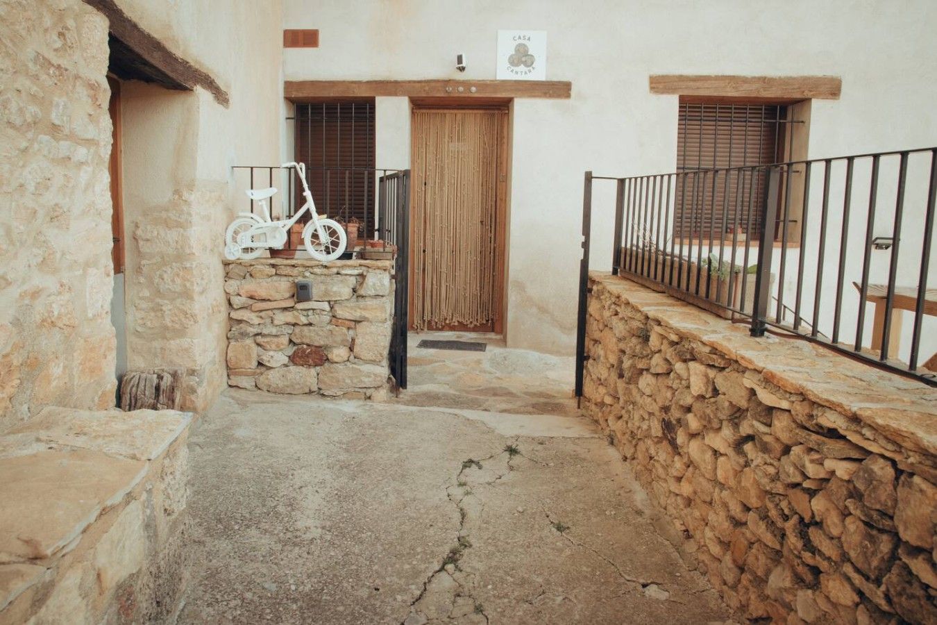 Un patio con paredes de piedra, una puerta de madera, una bicicleta blanca y una reja de metal.
